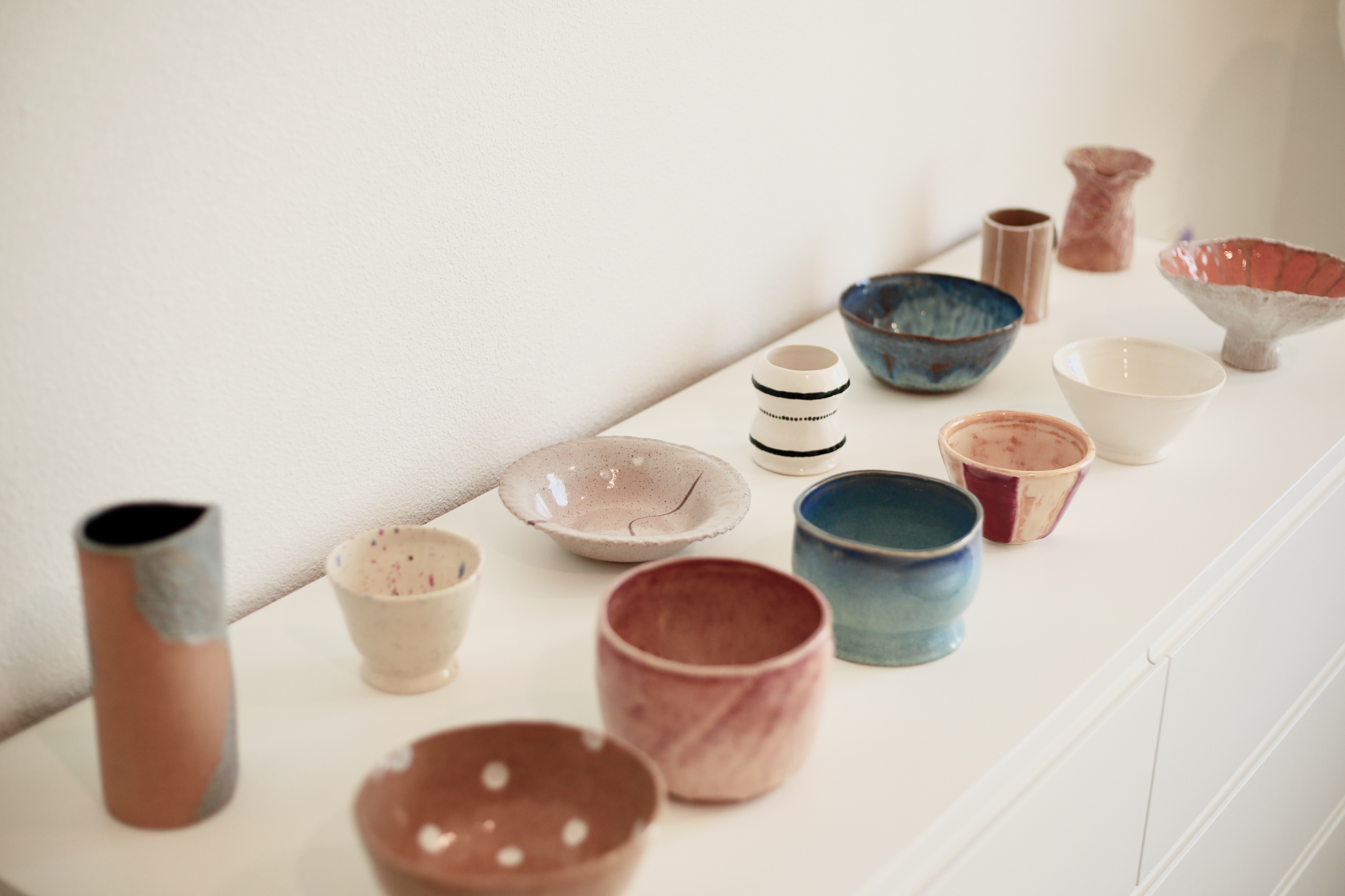 Handmade ceramics at home — bowls, plates and cups on a shelf